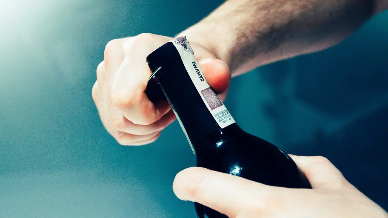 Dwie dłonie otwierają butelkę z winem domowym. Chcesz wiedzieć, jak zmierzyć zawartość alkoholu w winie domowym?
