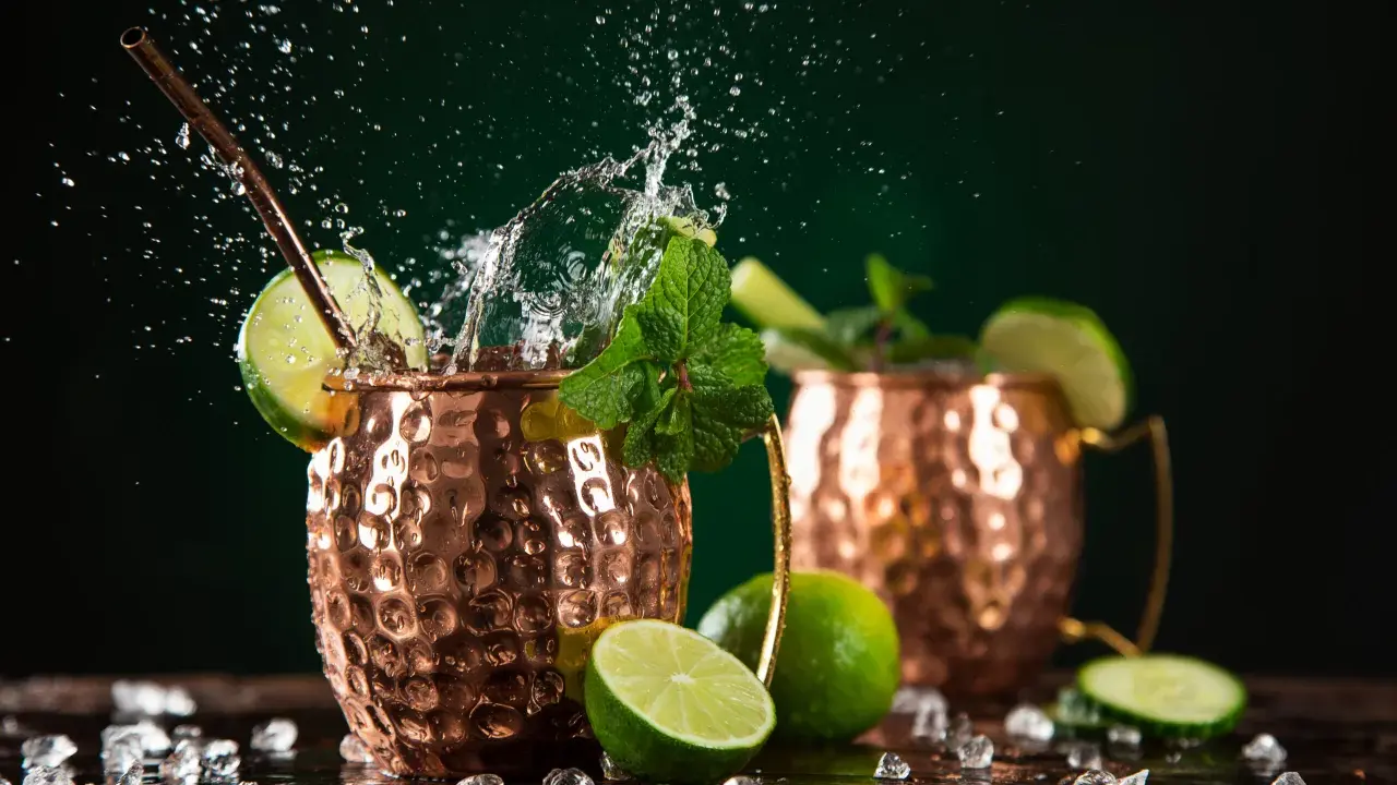 Orzeźwiający moscow mule drink z miętą i limonką, w miedzianych kubkach, z bryzgami wody i lodem.