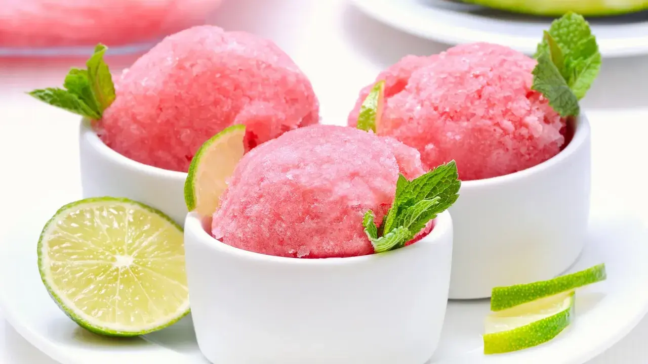 Orzeźwiający sorbet z arbuza w białych miseczkach, udekorowany listkami mięty i plasterkami limonki. Idealny na upalne dni.