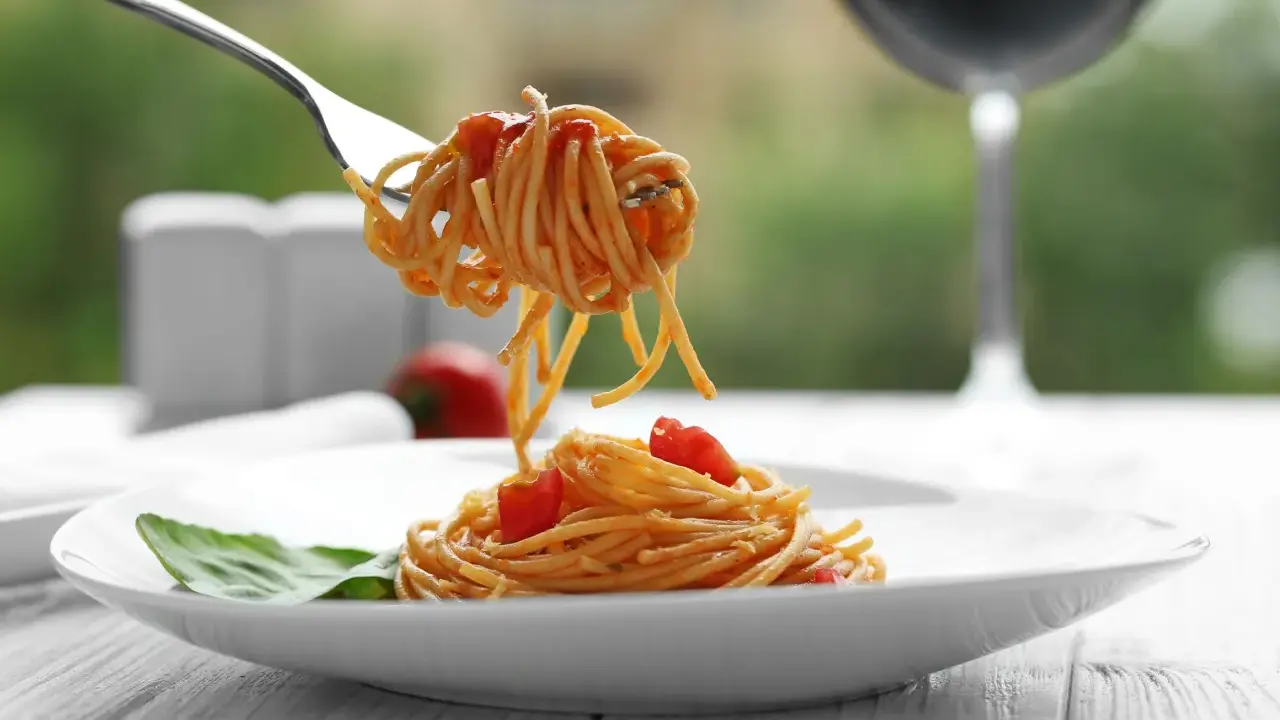 Idealne spaghetti z sosem pomidorowym na talerzu, a w tle kieliszek czerwonego wina. Zastanawiasz się, jakie wino do spaghetti wybrać?