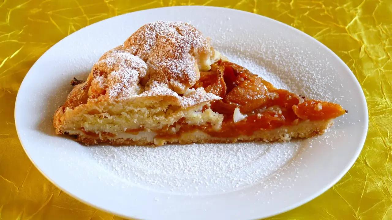 Pyszna tarta z morelami, posypana cukrem pudrem, na białym talerzu.