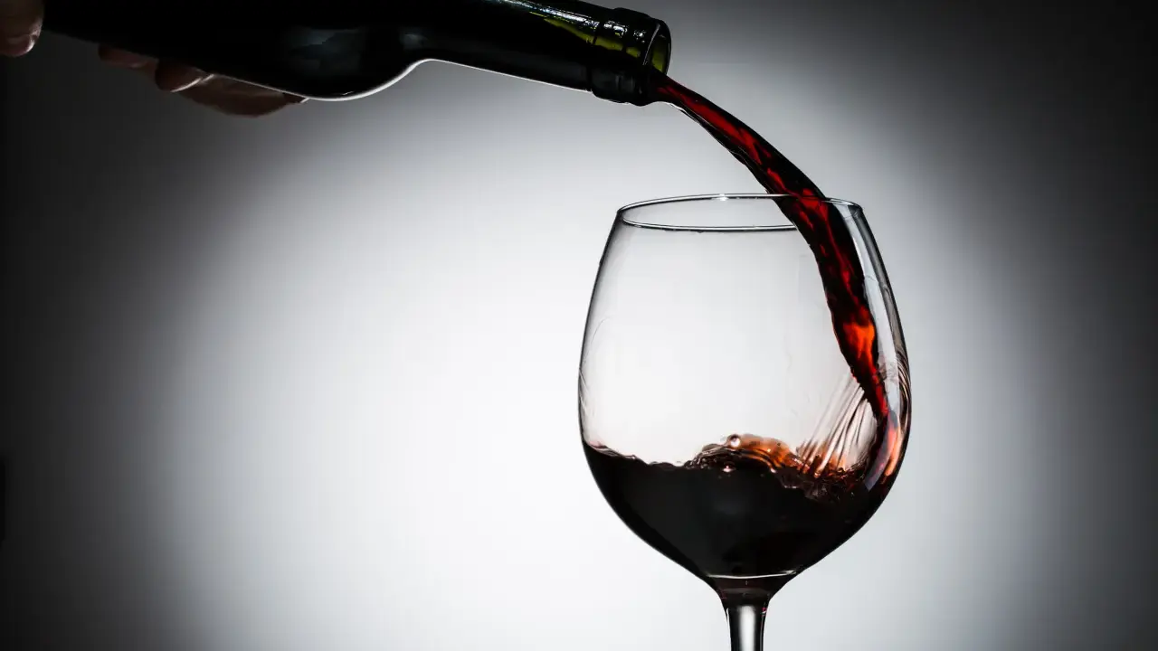 Czerwone wino leje się z butelki do kieliszka. Czy wino jest zdrowe? To pytanie towarzyszy tej chwili.