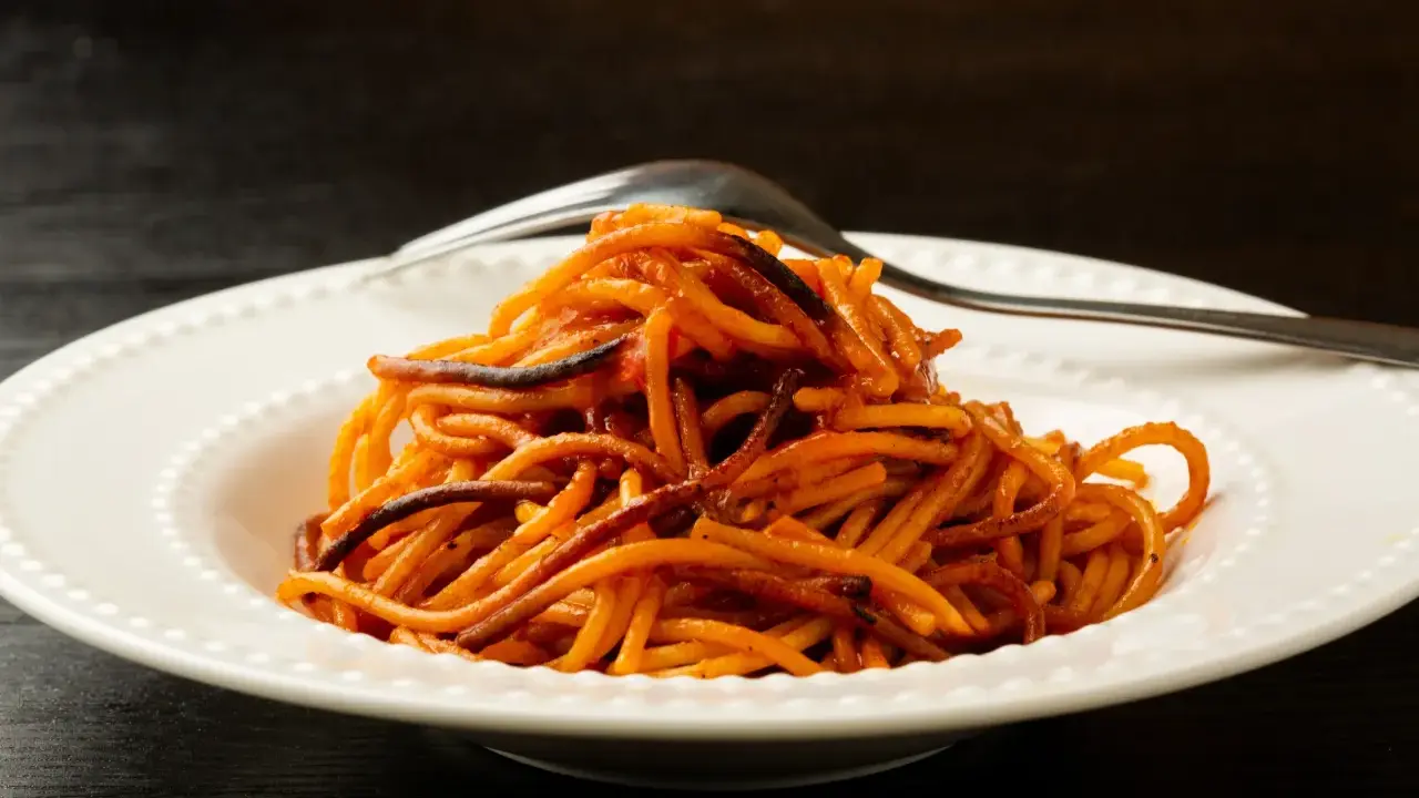 Spaghetti all'assassina, lekko przypalone, podane na białym talerzu z widelcem.