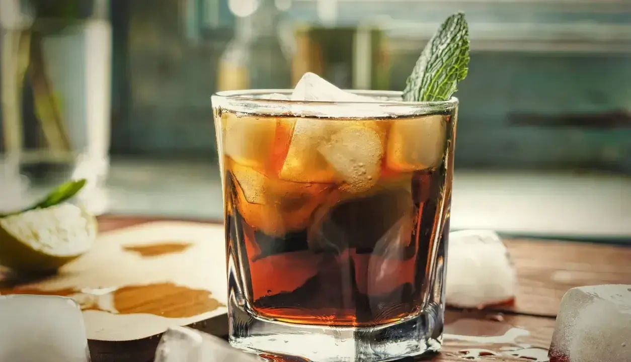 Orzeźwiający gin z colą, z lodem i miętą, na drewnianym blacie. Idealny na letnie wieczory.