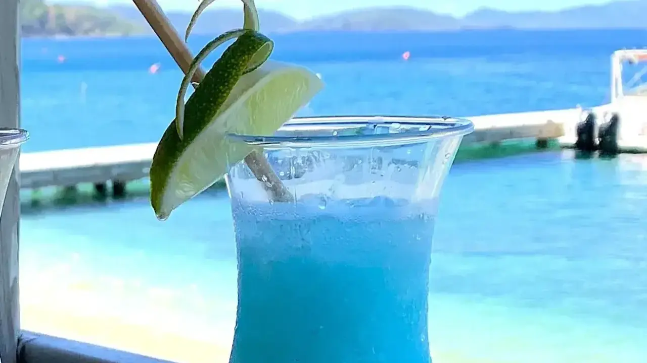 Niebieski drink z limonką, idealne proporcje Malibu z mlekiem, na tle błękitnego morza i plaży.