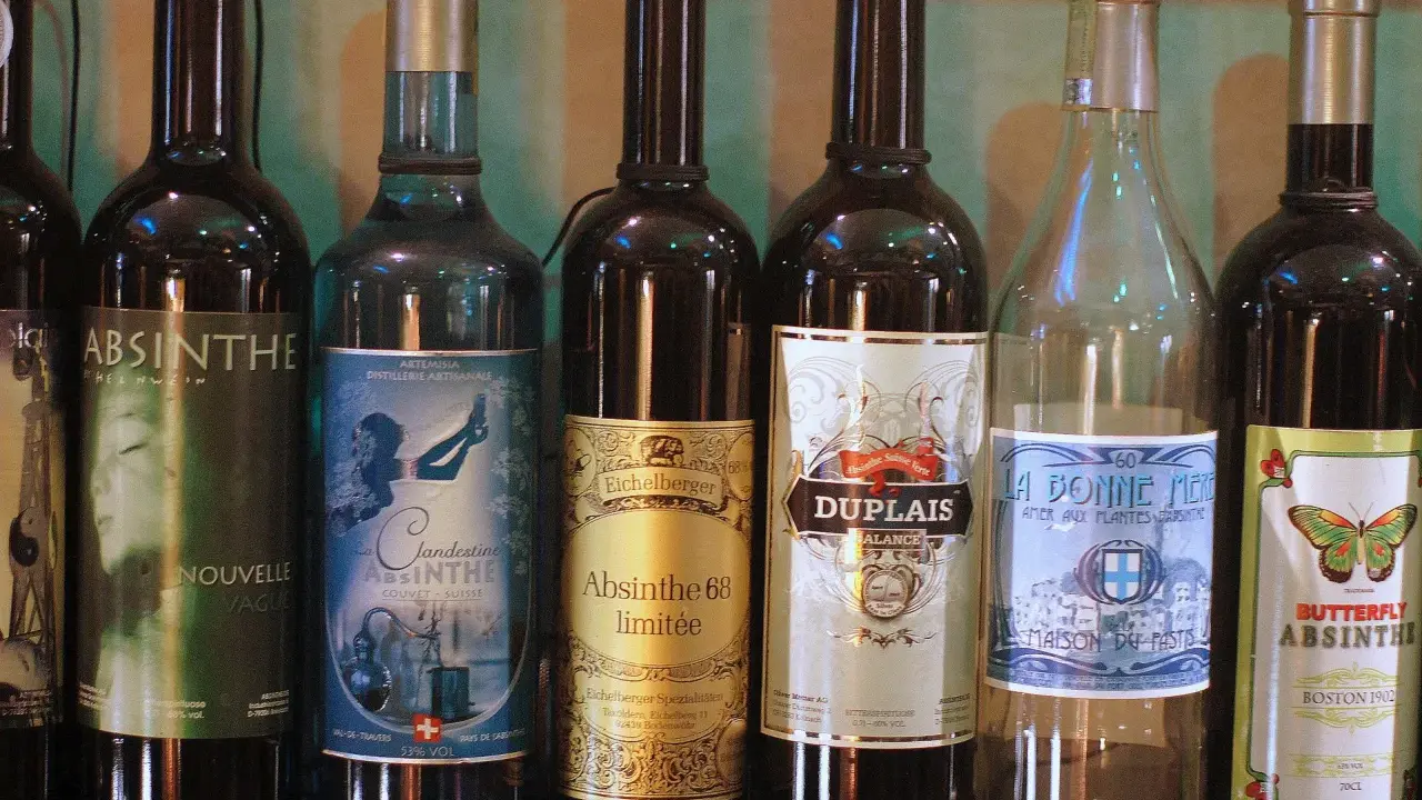 Rząd butelek z napisem "Absynt co to". Widać różne marki, m.in. Clandestine, Eichelberger, Duplais, La Bonne Mere, Butterfly Absinthe.