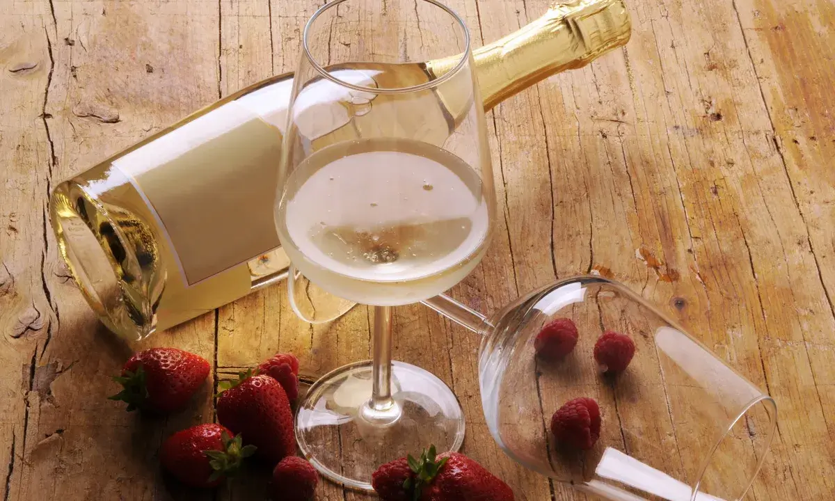 Butelka i kieliszki z winem musującym, obok truskawki i maliny. Idealne drinki z winem musującym na letnie popołudnie.