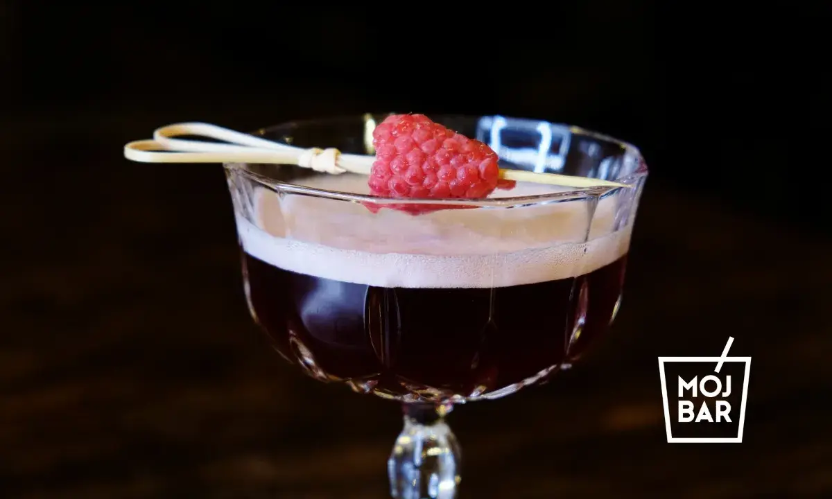 Elegancki koktajl Clover Club z maliną na patyczku, serwowany w kieliszku z logo MOJ BAR.
