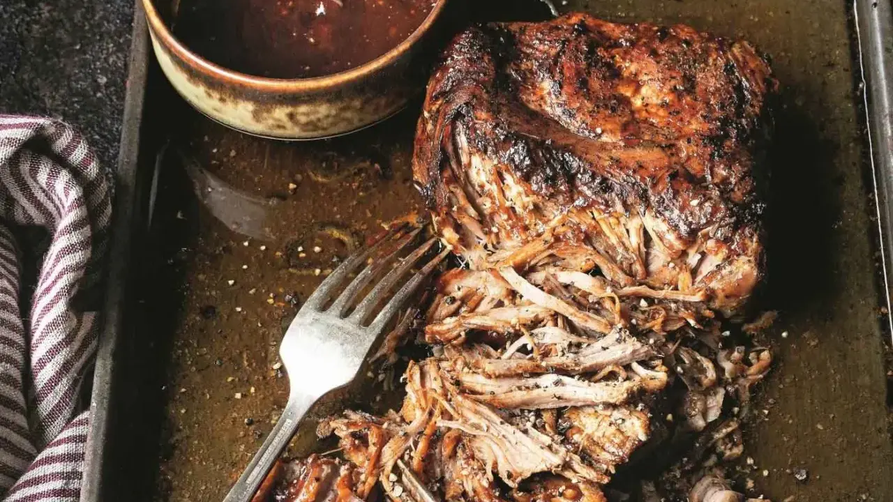 Soczyste pulled pork na blasze, gotowe do podania z sosem barbecue. Widoczne widelce ułatwiające rozrywanie mięsa.