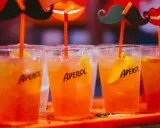 Idealne drinki na aperitif: orzeźwiające Aperole z lodem i plasterkiem pomarańczy, ozdobione zabawnymi wąsami i ustami.