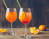 Dwa orzeźwiające aperol z prosecco, ozdobione plastrami pomarańczy i słomkami, na drewnianym blacie.
