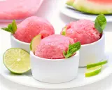 Orzeźwiający sorbet z arbuza w białych miseczkach, udekorowany listkami mięty i plasterkami limonki. Idealny na upalne dni.