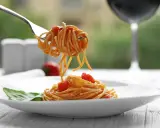 Idealne spaghetti z sosem pomidorowym na talerzu, a w tle kieliszek czerwonego wina. Zastanawiasz się, jakie wino do spaghetti wybrać?