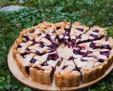 Pyszna tarta ze śliwkami, z kratką z ciasta, na drewnianej desce, wśród zielonej trawy.