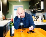 Zamyślony mężczyzna przy stole z winem i glukometrem. Czy czerwone wino obniża cukier?