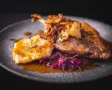 Pyszna pieczona gęś z chrupiącą skórką, podana z kluskami, czerwoną kapustą i chrupiącą cebulką. Idealne danie, do którego pasuje wino do gęsi.