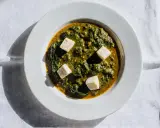 Palak paneer w białej misce, z kostkami sera paneer pływającymi w zielonym sosie ze szpinaku.