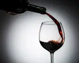 Czerwone wino leje się z butelki do kieliszka. Czy wino jest zdrowe? To pytanie towarzyszy tej chwili.