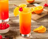 Dwa drinki tequila sunrise z pomarańczą i wiśnią, na drewnianym stole.