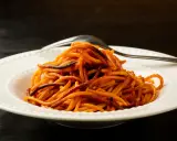 Spaghetti all'assassina, lekko przypalone, podane na białym talerzu z widelcem.