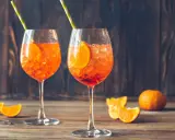 Dwa orzeźwiające drinki aperol ze sprite, udekorowane plasterkami pomarańczy i słomkami, na drewnianym tle.