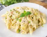 Penne z porem, groszkiem i szynką w kremowym sosie, posypane startym serem i udekorowane listkiem bazylii.