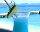 Niebieski drink z limonką, idealne proporcje Malibu z mlekiem, na tle błękitnego morza i plaży.