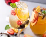 Orzeźwiający drink z prosecco, malinami, pomarańczą i miętą. Obok drugi napój z brzoskwinią i pomarańczą.