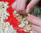 Ręce obierają świeże pestki dyni na czerwonej desce. Widać mnóstwo pestek i łupinek.