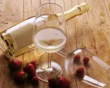 Butelka i kieliszki z winem musującym, obok truskawki i maliny. Idealne drinki z winem musującym na letnie popołudnie.