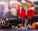 Dwa orzeźwiające drinki z białym winem, ozdobione plasterkami pomarańczy i miętą, stoją obok shakera i owoców.