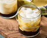 Dwa drinki White Russian z lodem i śmietanką, podane na drewnianej desce.
