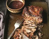 Soczyste pulled pork na blasze, gotowe do podania z sosem barbecue. Widoczne widelce ułatwiające rozrywanie mięsa.