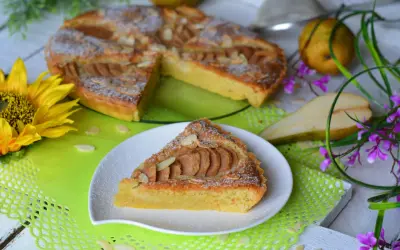 Pyszna tarta z gruszkami, posypana cukrem pudrem i płatkami migdałów, prezentuje się apetycznie na talerzyku. Obok cała tarta, gruszki i słonecznik.