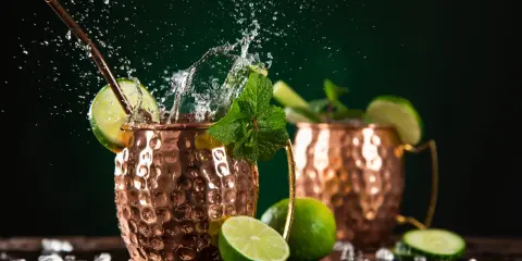 Orzeźwiający moscow mule drink z miętą i limonką, w miedzianych kubkach, z bryzgami wody i lodem.