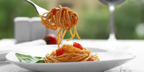 Idealne spaghetti z sosem pomidorowym na talerzu, a w tle kieliszek czerwonego wina. Zastanawiasz się, jakie wino do spaghetti wybrać?