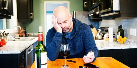 Zamyślony mężczyzna przy stole z winem i glukometrem. Czy czerwone wino obniża cukier?