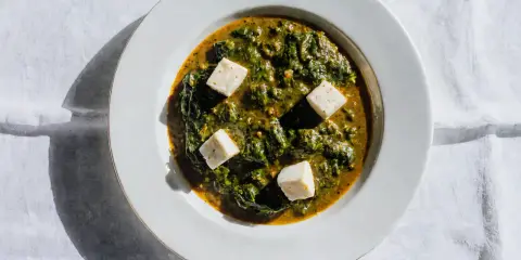 Palak paneer w białej misce, z kostkami sera paneer pływającymi w zielonym sosie ze szpinaku.