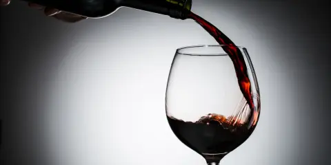 Czerwone wino leje się z butelki do kieliszka. Czy wino jest zdrowe? To pytanie towarzyszy tej chwili.