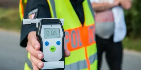 Policjant pokazuje alkomat z wynikiem 0.93 promila. Kierowca nie powinien wsiadać za kierownicę.