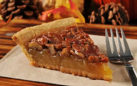 Kawałek pysznego, domowego pecan pie z orzechami i syropem, gotowy do zjedzenia.