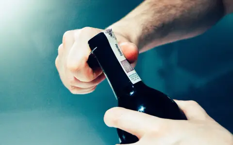 Dwie dłonie otwierają butelkę z winem domowym. Chcesz wiedzieć, jak zmierzyć zawartość alkoholu w winie domowym?