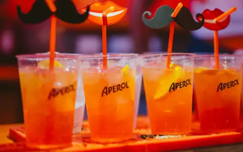 Idealne drinki na aperitif: orzeźwiające Aperole z lodem i plasterkiem pomarańczy, ozdobione zabawnymi wąsami i ustami.