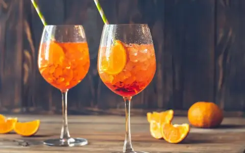 Dwa orzeźwiające aperol z prosecco, ozdobione plastrami pomarańczy i słomkami, na drewnianym blacie.