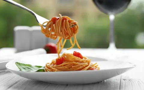Idealne spaghetti z sosem pomidorowym na talerzu, a w tle kieliszek czerwonego wina. Zastanawiasz się, jakie wino do spaghetti wybrać?