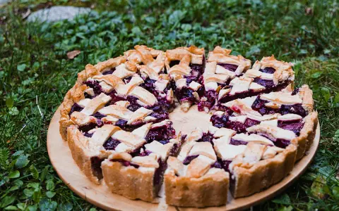 Pyszna tarta ze śliwkami, z kratką z ciasta, na drewnianej desce, wśród zielonej trawy.