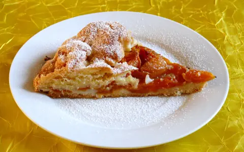 Pyszna tarta z morelami, posypana cukrem pudrem, na białym talerzu.