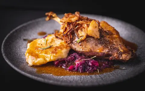 Pyszna pieczona gęś z chrupiącą skórką, podana z kluskami, czerwoną kapustą i chrupiącą cebulką. Idealne danie, do którego pasuje wino do gęsi.