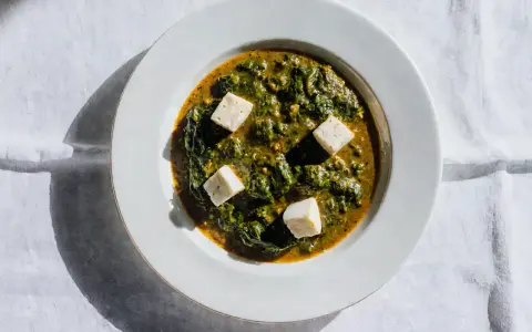 Palak paneer w białej misce, z kostkami sera paneer pływającymi w zielonym sosie ze szpinaku.