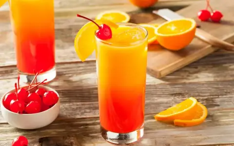 Dwa drinki tequila sunrise z pomarańczą i wiśnią, na drewnianym stole.